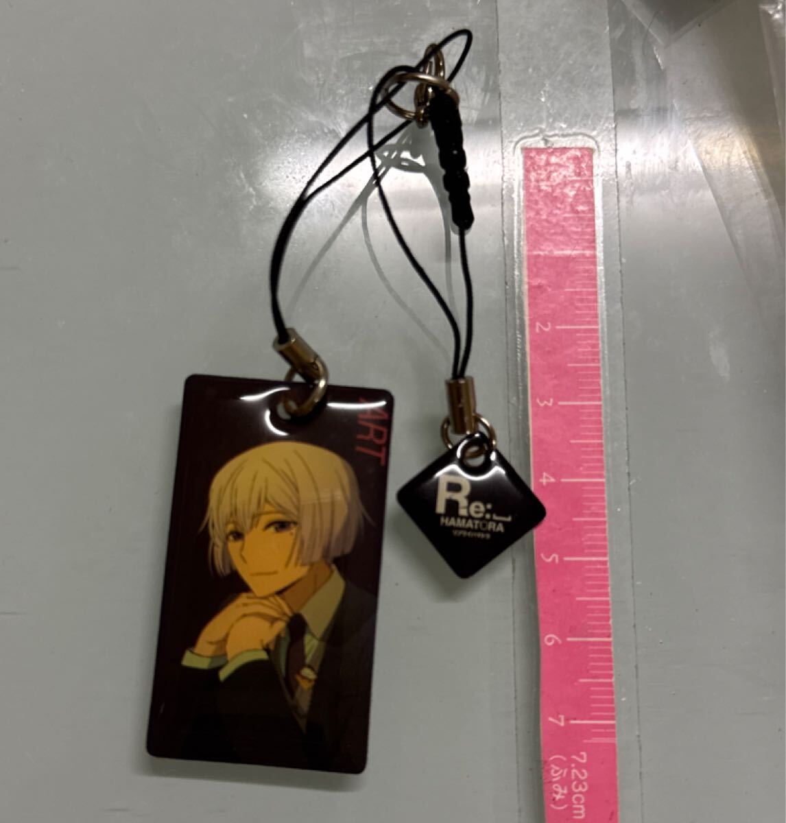 『Re: ハマトラ』のアートが描かれたプレートと、作品ロゴ「Re: HAMATORA」がデザインされた小さなパーツが組み合わされています。ART拍卖